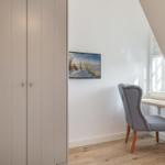 Schreibtisch mit Stuhl unter Fenster, Wandbild und Kleiderschrank im Raum.