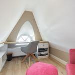 Dachgeschosszimmer mit Schreibtisch, rosa Sitzbank und Bogenfenster.
