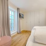 Schlafzimmer mit Bett, rosa Sessel, Fenster und Kleiderschrank.