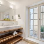 Badezimmer mit Holzwaschtisch, Spiegel und französischem Fenster.
