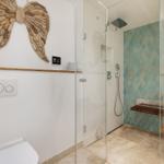 Dusche mit Glaswand, Holzbank und blauen Fliesen. Wanddekoration aus Holz.