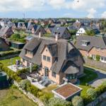 Haus mit Strohdach, Garten und Terrasse. Blick auf Wohnsiedlung und Hügel.