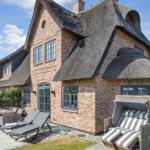 Haus mit Strohdach, Terrasse und Liegestühle im Garten.