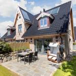 Haus mit Steinmauer, Terrasse und Garten. Holzveranda und Sitzgruppe im Freien.