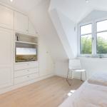 Schlafzimmer mit Dachschrägen, weißer Einbauschränke, Fernseher und Fenster mit Blick auf Bäume.