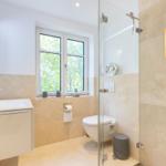 Badezimmer mit Dusche, Waschbecken und Fenster mit Blick auf Bäume.