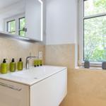 Badezimmer mit Waschbecken, Spiegel und Fenster mit Blick auf Bäume.