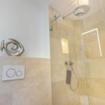 Dusche mit Glaswand und moderner Duschkopf. Wand mit Toilettensteuerung und Skulptur.