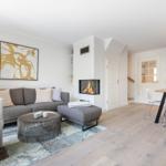 Wohnzimmer mit Sofa, Kamin und Esstisch. Holzboden und Wandbild sichtbar.