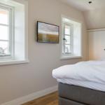 Bedroom with bed, TV, and two windows.
