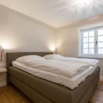 Bedroom with double bed, window, and wall lamp.