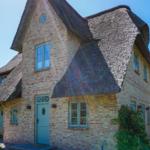 A house with thatched roof and brick facade. Door and windows are light blue.