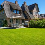 House with thatched roof, garden with seating and flower beds.