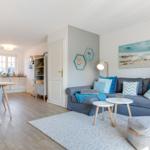Wohnbereich mit Sofa, Tischen und Küchenbereich im Hintergrund.