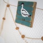 Wooden panel with bird motif hangs on fishing net with wooden beads.
