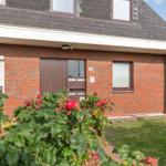 Red brick house with entrance door and windows. Front garden with rose hedge.