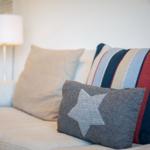 A sofa with striped and star-patterned cushions. Background: lamp and kitchen area.