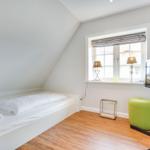 Schlafzimmer mit Bett, Fenster und Fernseher auf Ständer.