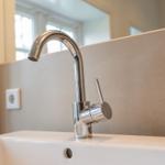 Moderne Waschbecken mit chromfarbenem Wasserhahn und Spiegelfläche im Hintergrund.