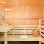 Sauna mit Holzbänken, Thermometer und Eimer mit Löffel.