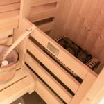 Sauna mit Holzbank, Steinboden und Eimer mit Holzlöffel.