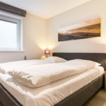 Schlafzimmer mit Doppelbett, Fenster und Nachttisch mit Lampe.