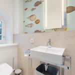 Badezimmer mit Fischmotivwand, Waschbecken und Toilette unter einem Bogenfenster.