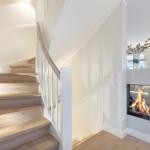 Holzgetreppe mit weißem Geländer und Kamin im Wohnbereich.