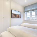 Schlafzimmer mit weißem Bett, Fenster und Wandbild.