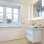 Badezimmer mit Dusche, Waschbecken und Fenster mit Blick auf Bäume.