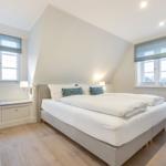 Schlafzimmer mit Doppelbett, zwei Fenstern und Holzboden.