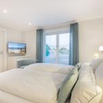 Schlafzimmer mit Blick auf Strand, TV und Bett mit Kissen.