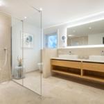 Moderne Dusche mit Glaswand, zwei Waschbecken und Spiegelschrank.