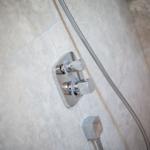 Duschbereich mit chromfarbenen Armaturen und Fliesenwand