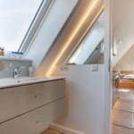 Duschbad mit Dachfenster und Spiegelschrank. Blick in Schlafzimmer mit Holzboden.