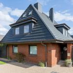 Ferienhaus mit rotem Backstein und dunklem Dach, Eingang mit Schild und Gartenbereich.