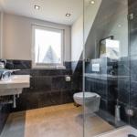 Bathroom with shower, toilet, and sink. Black marble wall and window with view.