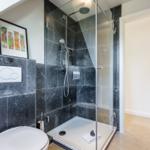 Shower with glass enclosure, toilet, and wall art in modern bathroom