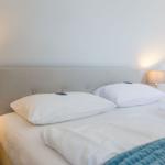 Double bed with white pillows and bedding. Wooden nightstand and lamp.