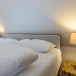 Double bed with white pillows and bedding under slanted walls with nightstands and lamps.