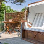 Wooden terrace with beach chair, table, and plants. Background: wooden fence and trees.