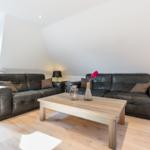 Two dark leather sofas surround a wooden table. Wooden floor and white walls.