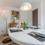 Round table with dishes and bottles. Transparent chairs and wall art.
