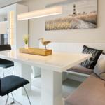 Dining area with white table, bench, and wall art with lamp.