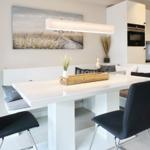 Dining area with white table, dark chairs, and bench. Wall art and ceiling light.