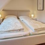 Double bed with two mattresses and white bedding under sloped ceiling