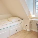 Bedroom with sloped ceiling, bed, desk, and window.