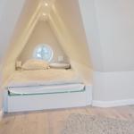 Bedroom with sloped ceiling, round window, and white bed.