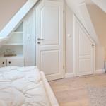 Bedroom with sloped ceilings, white door, and bed with white bedding.