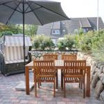 Terrace with table, chairs, and umbrella. Background: garden with stone wall and house.